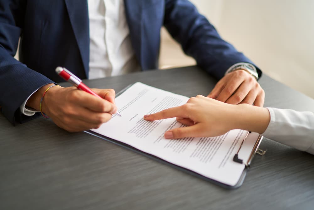 A close-up of a client in a business suit holding a pen to sign a contract on a clipboard while a loan officer points to the signature line, representing the approval process for summit financial loans.